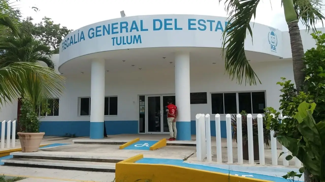Front view of the Fiscalía General del Estado office in Tulum with a person entering the building and tropical vegetation surrounding it.