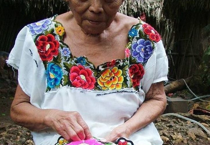 An elderly woman with a richly embroidered traditional blouse is sewing by hand outdoors.