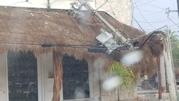 Utility pole transformer sparks over a thatched roof, causing a shower of sparks while a utility worker operates a cherry picker nearby.