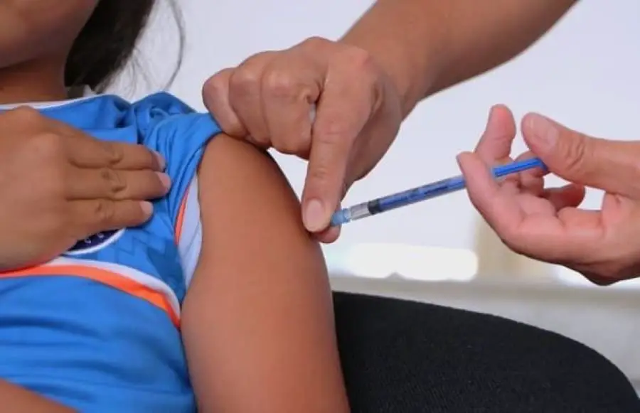 A healthcare professional administering a vaccine to a child who is wearing a blue shirt