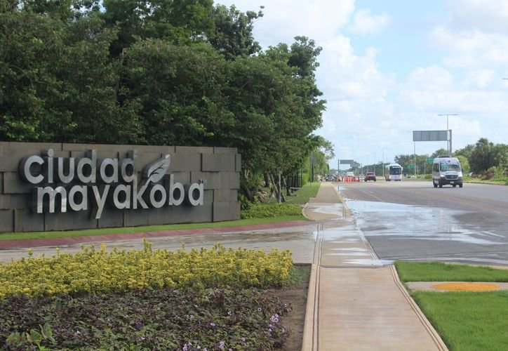 Entrance sign of Ciudad Mayakoba beside a road with a vehicle and lush greenery around.