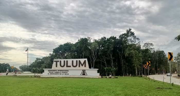 The entrance sign of Tulum, with the word 'TULUM' in large letters, surrounded by lush greenery, signaling the entrance to the archaeological site in Mexico.