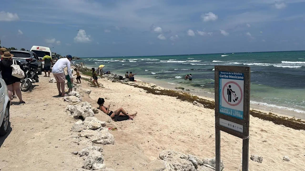 People enjoying a sunny day at a tropical beach with waves in the background and a 'Do Not Litter' sign in the foreground.