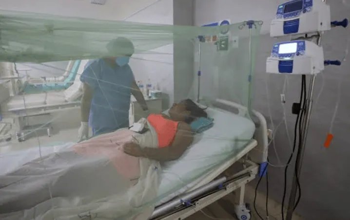 A healthcare worker attends to a patient lying in a hospital bed equipped with medical devices.