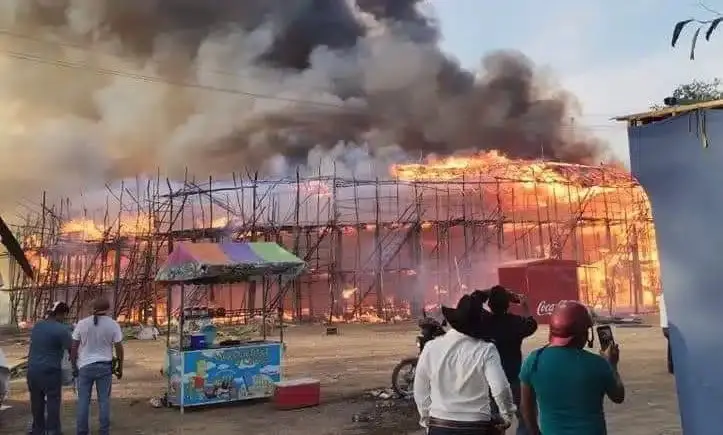 A large fire consumes a building with scaffolding as onlookers watch and some take photos; thick smoke rises into the sky.