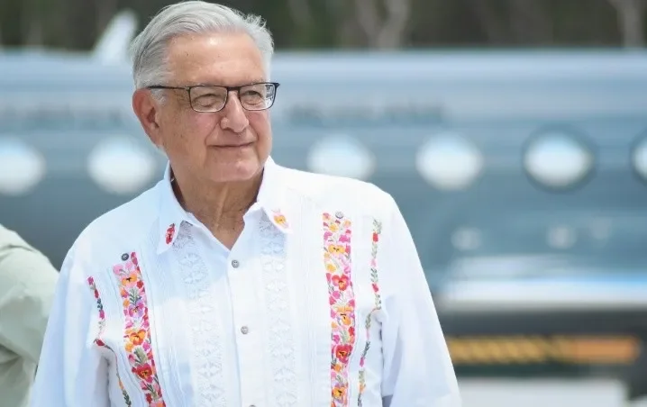 An elderly man wearing glasses and a traditional white embroidered shirt smiling subtly with a blurred background.