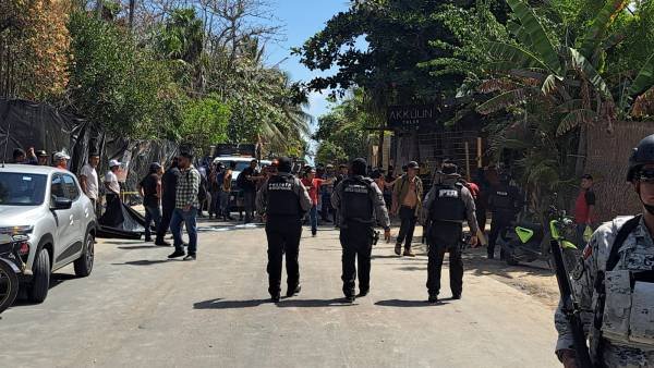 Police and security personnel on a closed road with bystanders and vehicles on the sidelines.