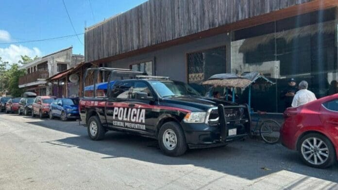 A police vehicle parked on the side of a street with various cars lined up and a building with umbrellas shading outdoor tables in the background.