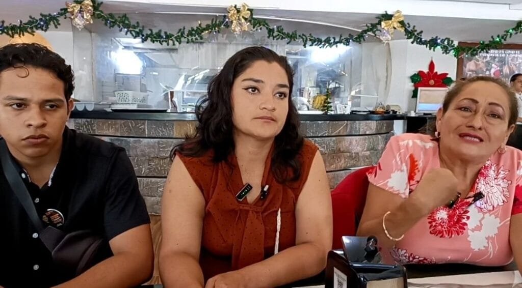 Three people sitting at a table in a restaurant decorated for the holidays, appearing to be in the midst of a conversation.
