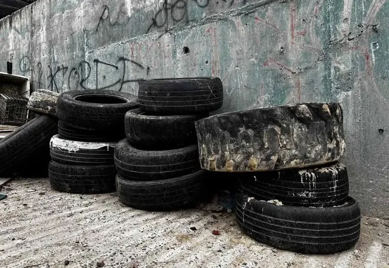 A pile of worn-out and abandoned tires against a concrete wall with graffiti.