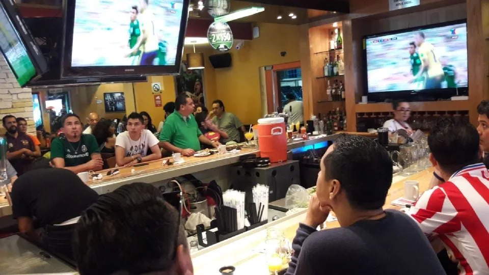 A lively bar scene with patrons watching a soccer match on multiple screens, focused on the game and enjoying drinks.$#$ CAPTION