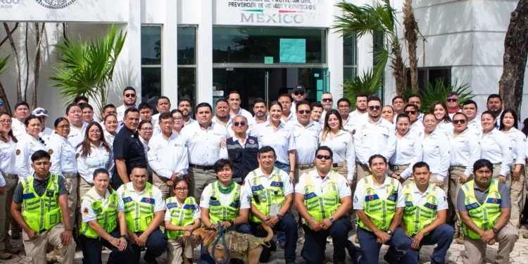 A large group of emergency services personnel posing for a photo outside a building in Mexico, wearing uniforms and casual attire, with some holding a service dog.$# CAPTION