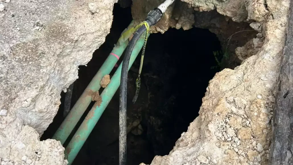 A close-up of a large hole in the ground revealing various cables and pipes underneath a rocky surface.$#$ CAPTION