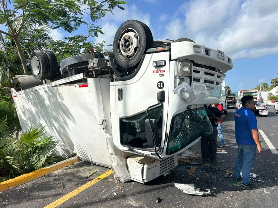 An overturned delivery truck lies on its side next to a road, with emergency responders and bystanders present.$# CAPTION