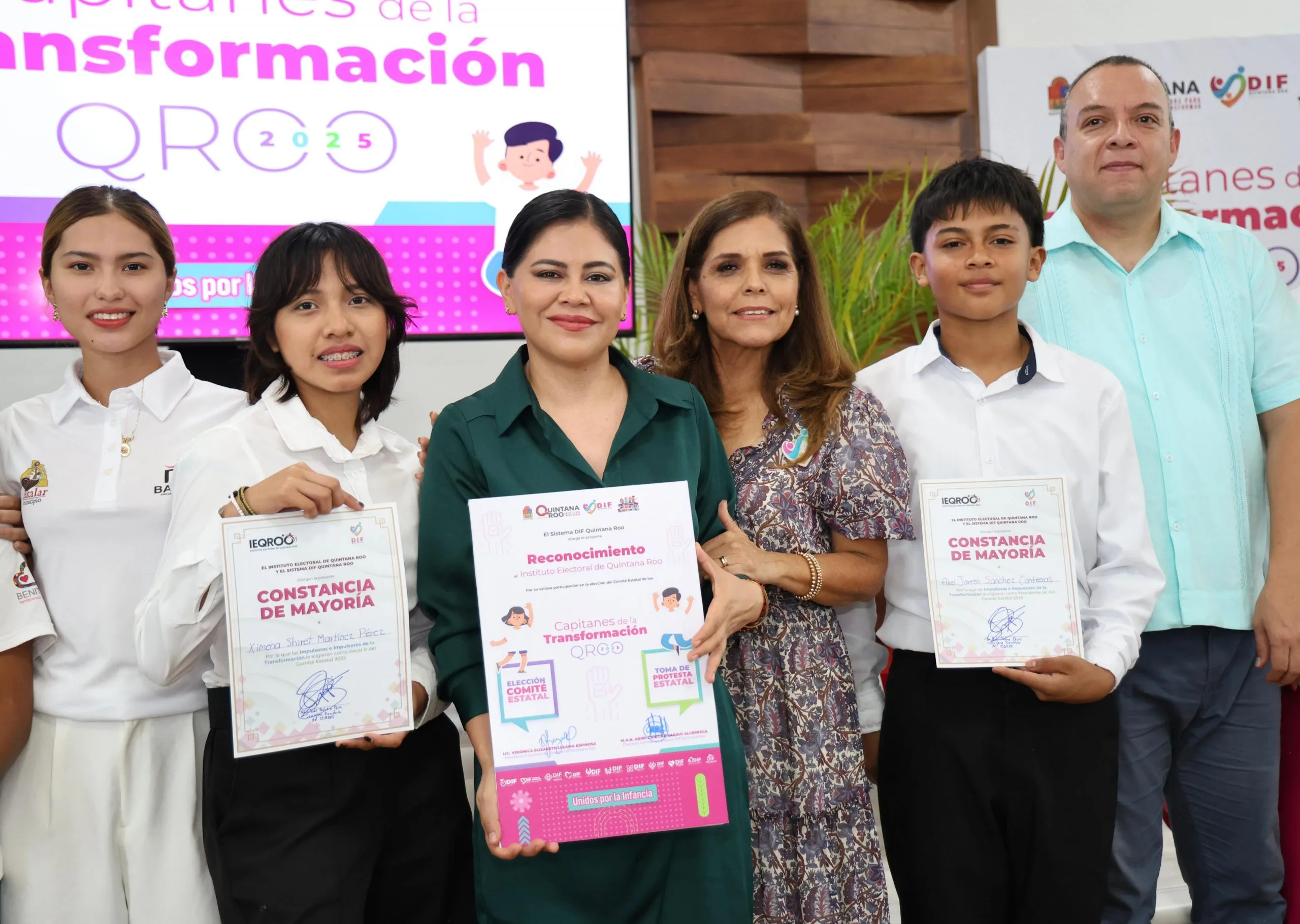 A group of youth holding certificates at a recognition event in Quintana Roo, with officials in the background.$# CAPTION