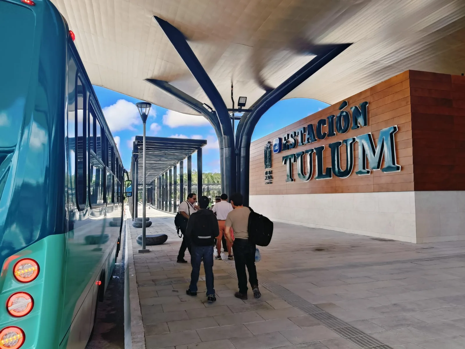 People gathering at the Tulum Bus Station with a turquoise bus parked nearby.