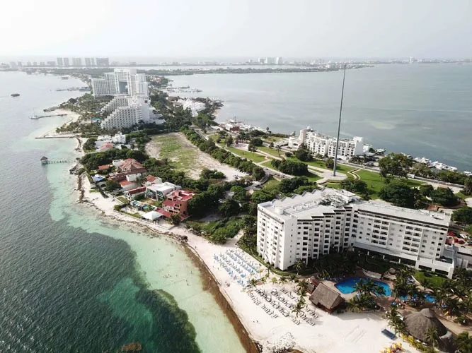 A bird’s-eye view of a coastal resort area featuring a blend of hotels, lush greenery, and sandy beaches with clear blue waters.$#$ CAPTION
