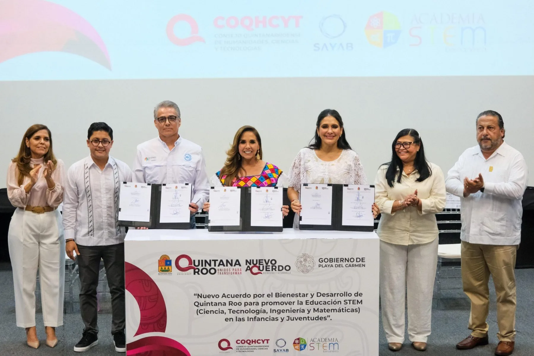 Group of officials and representatives at a signing ceremony for a new agreement on STEM education in Quintana Roo, Mexico. Several documents are displayed on a table.