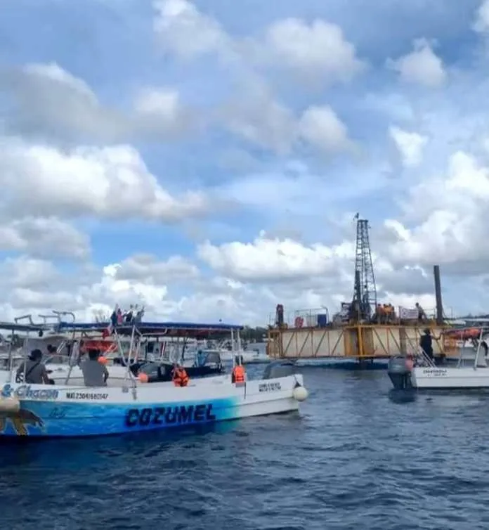 Several boats are sailing in the water near an offshore platform under a cloudy sky in Cozumel.$#$ CAPTION
