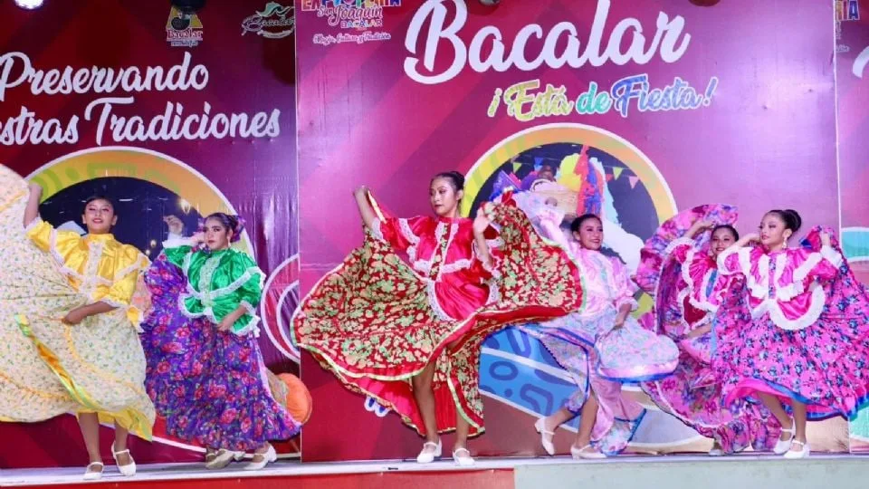 A vibrant performance featuring dancers in traditional costumes during a cultural event in Bacalar, showcasing colorful dresses and lively movement on stage.$# CAPTION