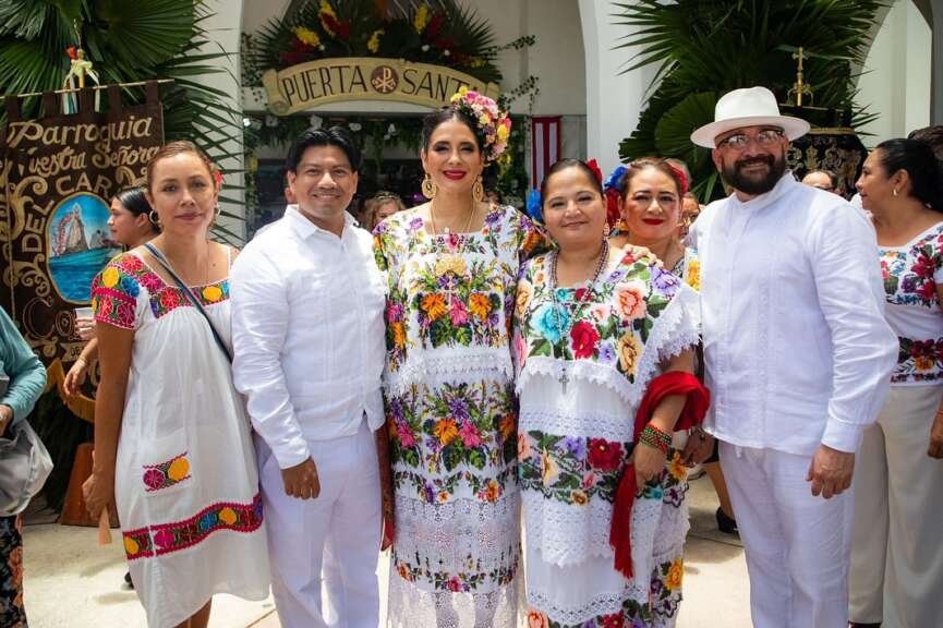 A group of individuals dressed in colorful traditional outfits poses for a photo in front of a sign that reads "Puerta Santa."