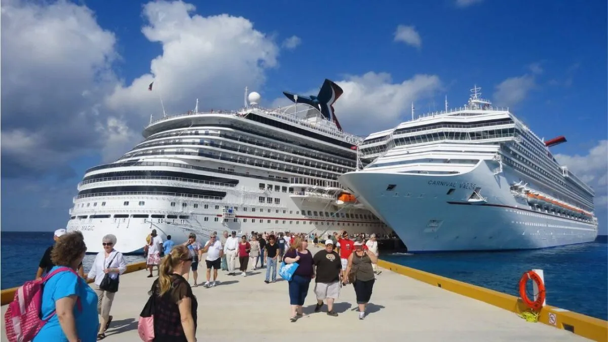Two large cruise ships docked at a port with tourists walking nearby under a blue sky with clouds