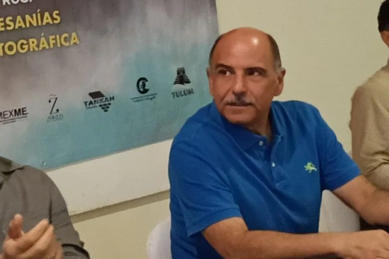A man in a blue polo shirt sitting among others, participating in a discussion at a community meeting.