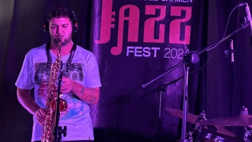 A saxophonist playing on stage at a jazz festival, with a backdrop featuring the festival logo and name in bold letters.$#$ CAPTION