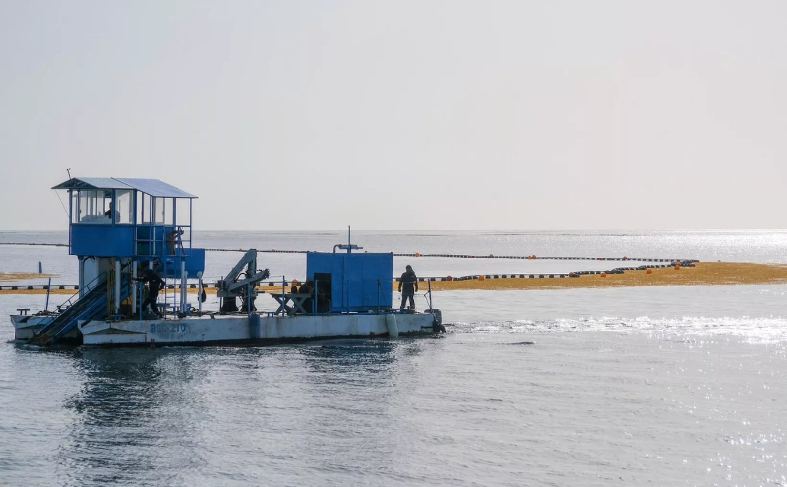 A blue vessel conducting maintenance work on the water with crew members present on board.$# CAPTION