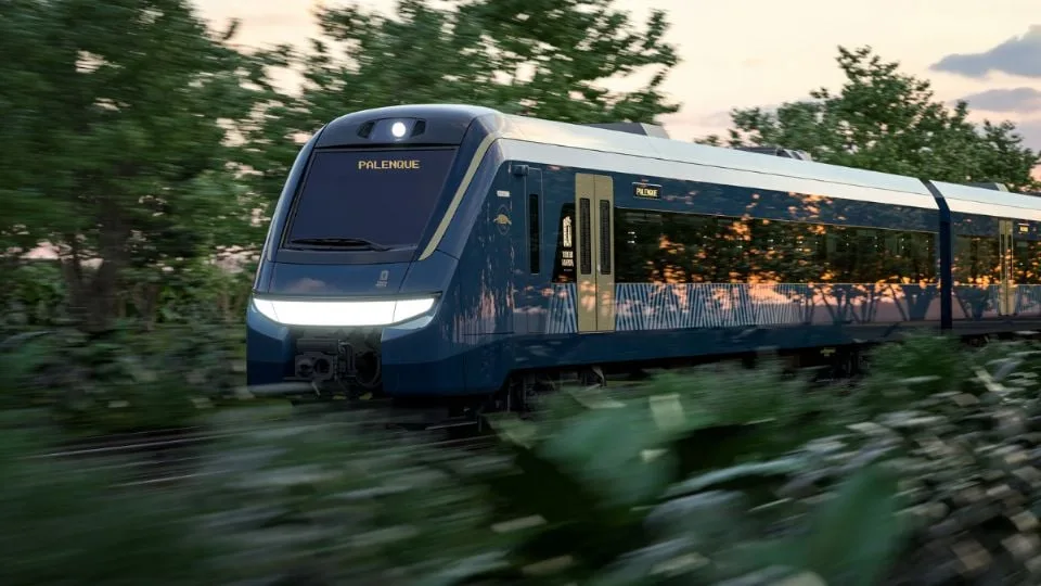 A sleek blue train labeled "Palenque" moving through scenic greenery at sunset
