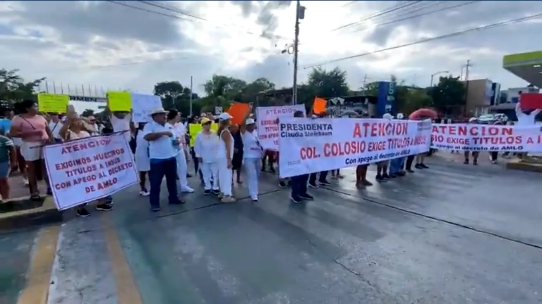A group of protesters holding banners demanding land titles in Colonia Colosio, accompanied by colorful signs, during a demonstration in the street.$# CAPTION