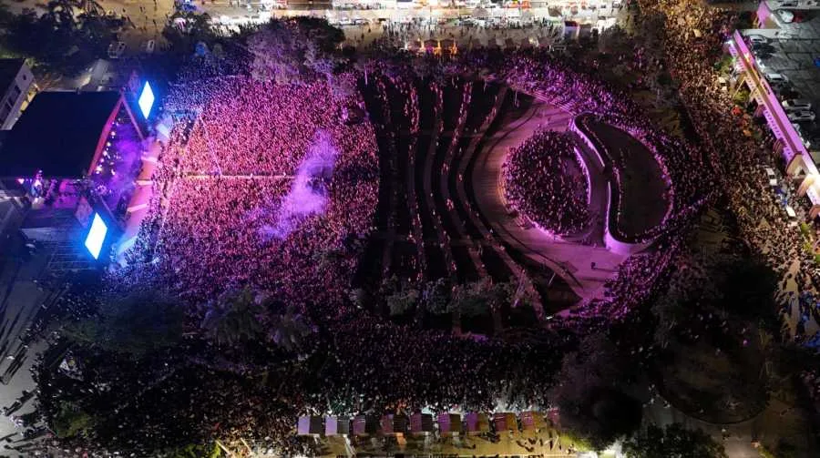 Aerial view of a massive crowd at a concert, with colorful lights illuminating the scene and a stage visible on the left side.$# CAPTION