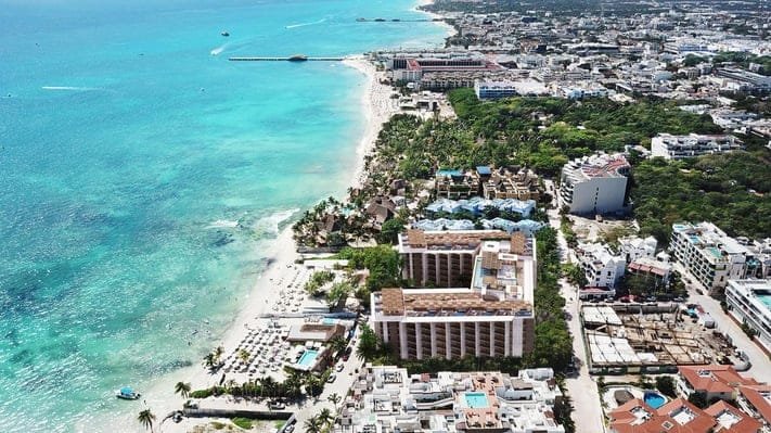 A panoramic aerial view of a coastal resort area featuring a beach, hotels, and turquoise waters