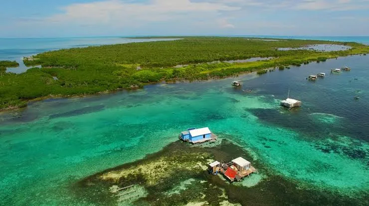 Aerial view of clear turquoise waters with mangrove islands and small structures on the water's surface