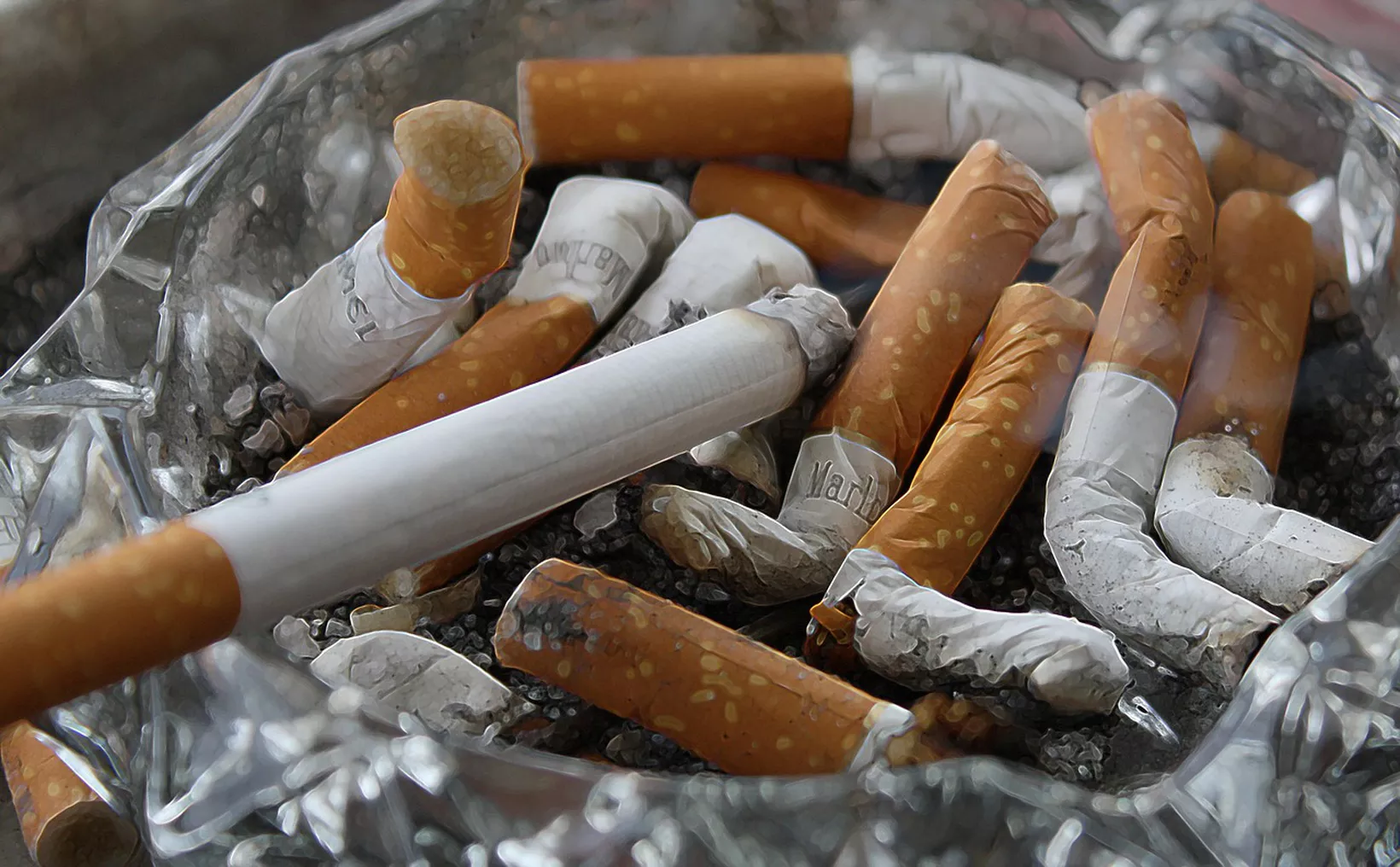 Close-up view of an ashtray filled with used and unused cigarettes, some with burnt ends and others unlit, surrounded by ash and debris.