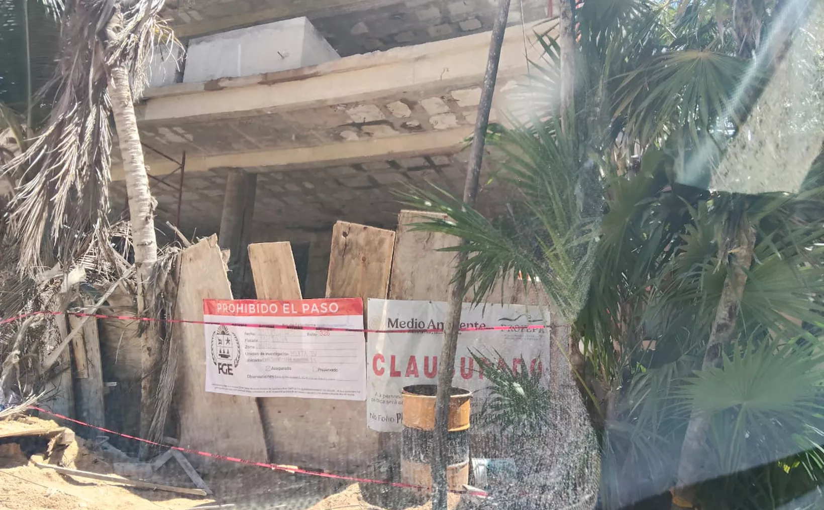 A partially constructed building surrounded by warning signs and barriers, with palm trees in the foreground.$# CAPTION