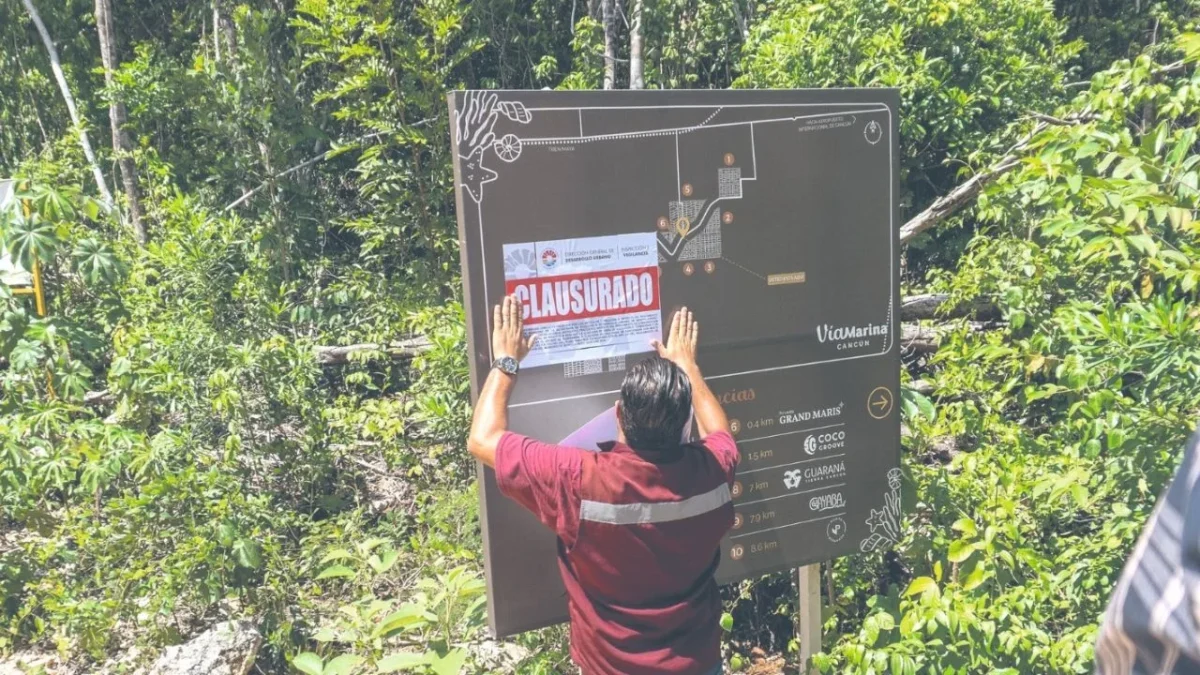 A person affixing a 'CLOSED' notice to a map sign in a dense green environment