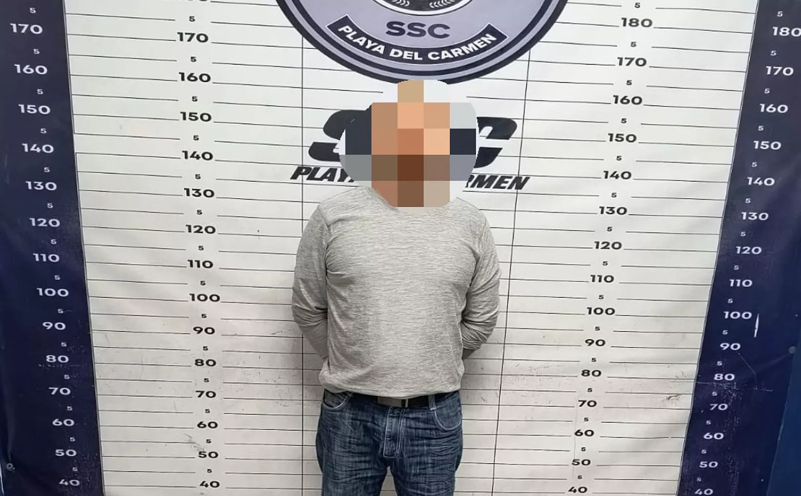 A person standing in front of a height measurement board marked with various height indicators in Playa del Carmen, showing numbers from 40 to 180 centimeters, with their identity obscured for privacy.$$# CAPTION