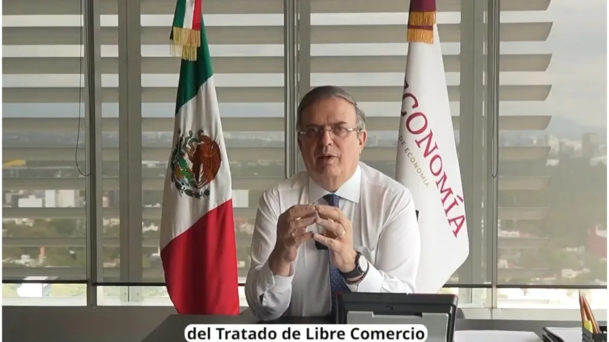 A man speaking in an office with the Mexican flag and an "Economía" banner behind him.$# CAPTION