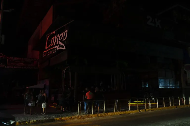 A dimly lit exterior view of Congo Bar in Cancun, with a few people standing outside in the darkened street.$# CAPTION