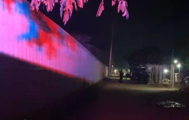 A dimly lit street at night with colorful lights projected on a wall and police officers in the distance. A vehicle is also visible.