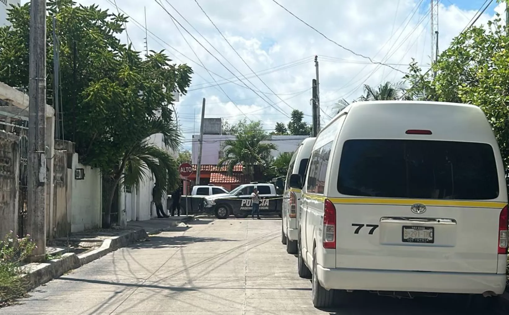 A police vehicle and a few white vans parked on a quiet street surrounded by greenery and a stop sign in the background.$#$ CAPTION