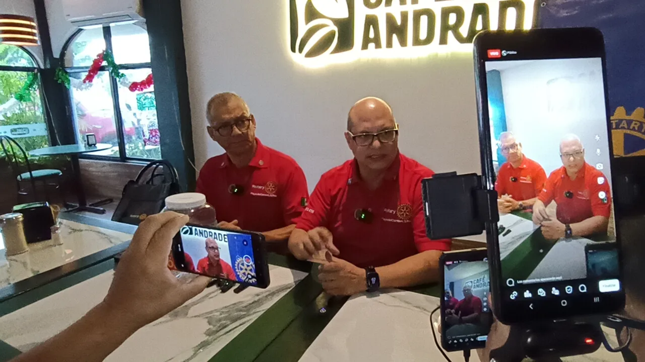 A press conference featuring three speakers in red shirts at Café Andrade, with attendees holding smartphones to capture the event.$# CAPTION