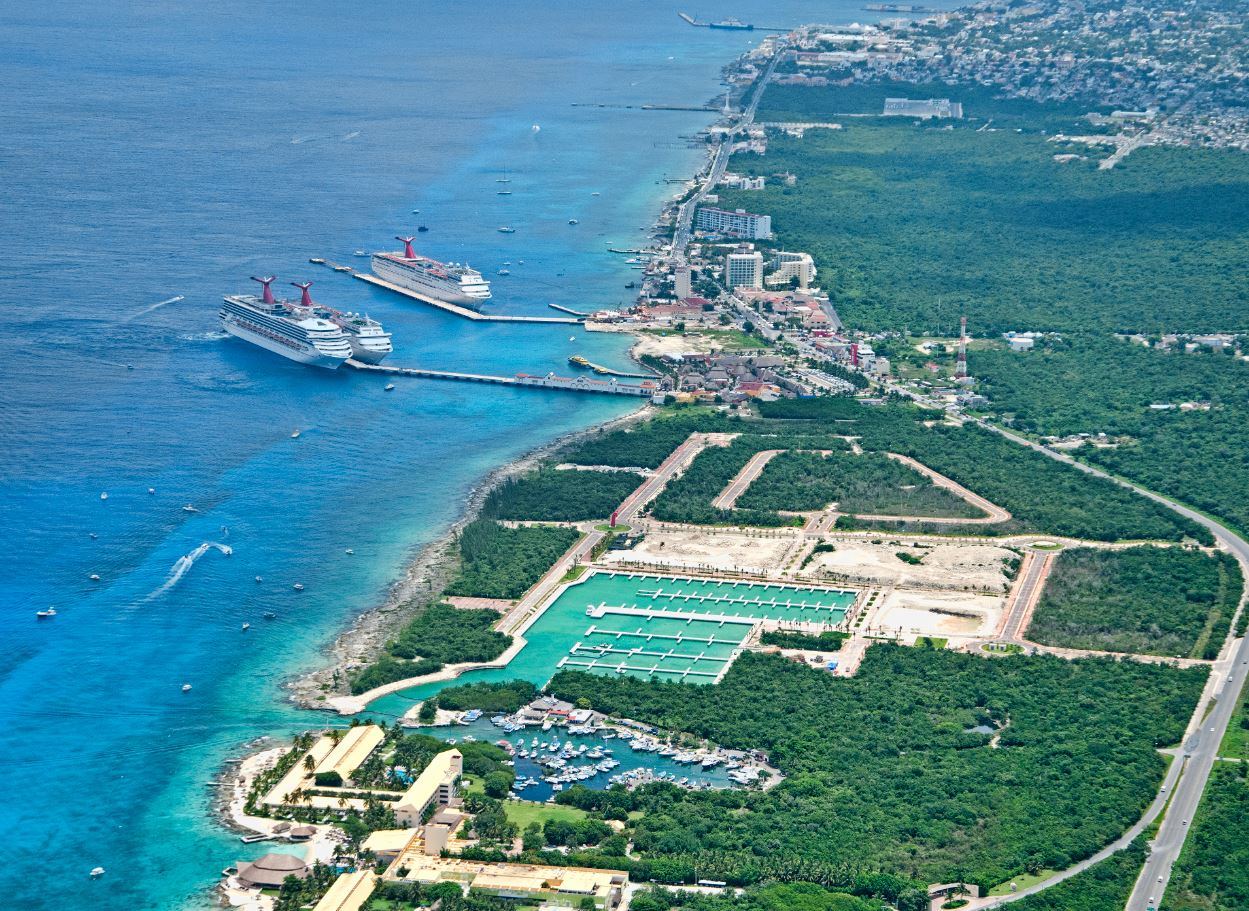 aerial view showing cruise ships docked at a pier with a marina and lush greenery in the background