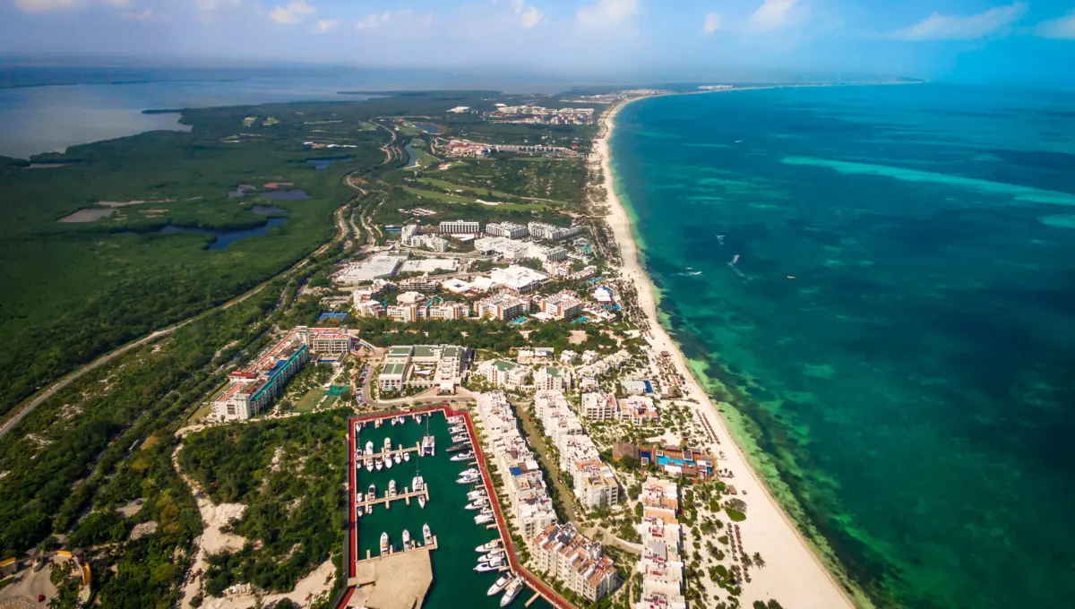 Aerial view of a coastal resort with a marina, lush greenery, and turquoise waters in the background