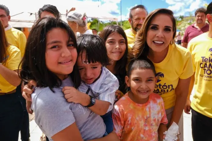 A group of children and an adult woman smiling together during a community event, all wearing bright clothing.$#$ CAPTION