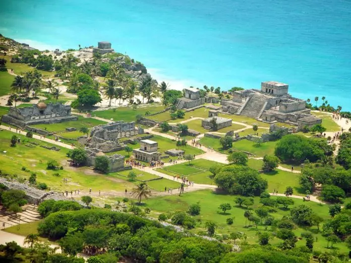 An aerial view of ancient ruins surrounded by lush greenery and a vibrant blue ocean.