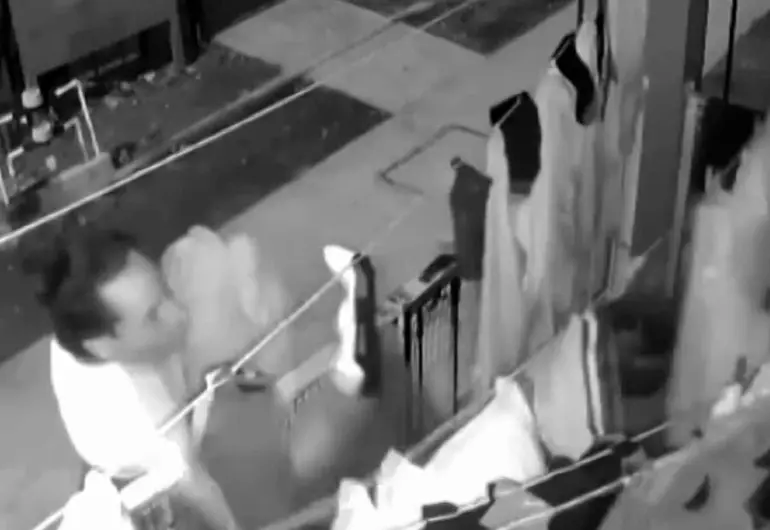 A black and white image showing a person near a clothesline, appearing to interact with clothes hanging on it in a street setting.$#$ CAPTION