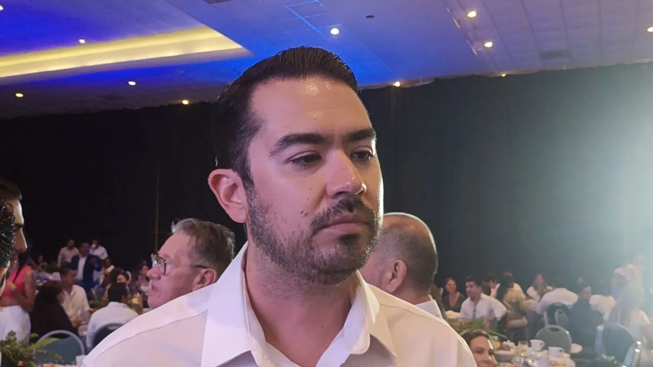 A man with dark hair and a neatly groomed beard, wearing a white shirt, is seen in a crowded venue filled with people enjoying a social event. The background features a dimly lit setting with party tables and decorations.$#$ CAPTION