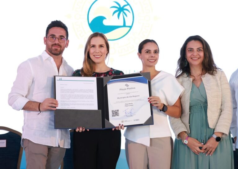 A group of four individuals proudly holding a Playa Platino certification during an event. Two men and two women are dressed in formal attire, standing together in front of a branded backdrop. The woman in the center holds the certificate prominently.